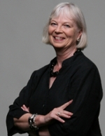 A woman with short white hair smiles while crossing her arms.