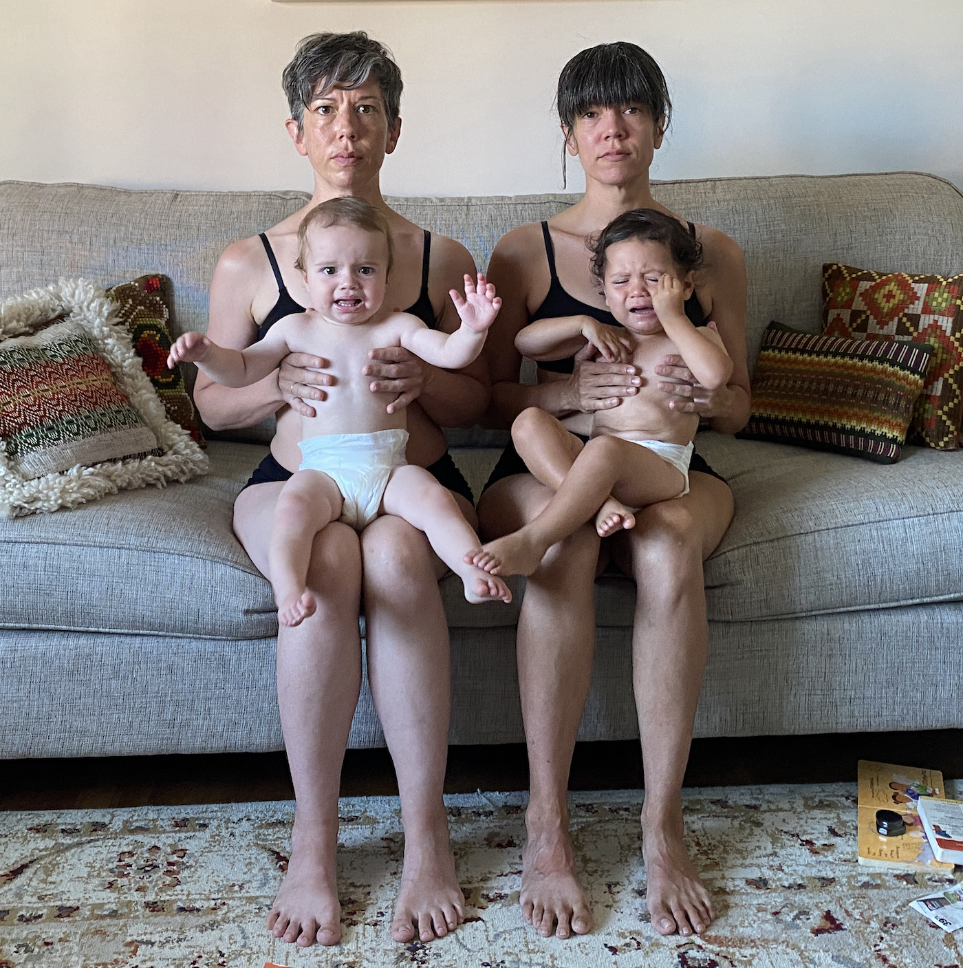 Two women sat on a couch, each holding a baby on their lap